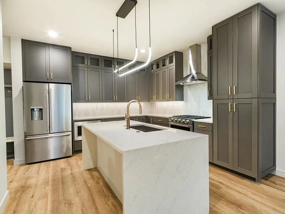 Designer kitchens feature quartz waterfall islands, full-height cabinetry, stainless steel appliances, and modern lighting that create a sophisticated space for cooking and entertaining.