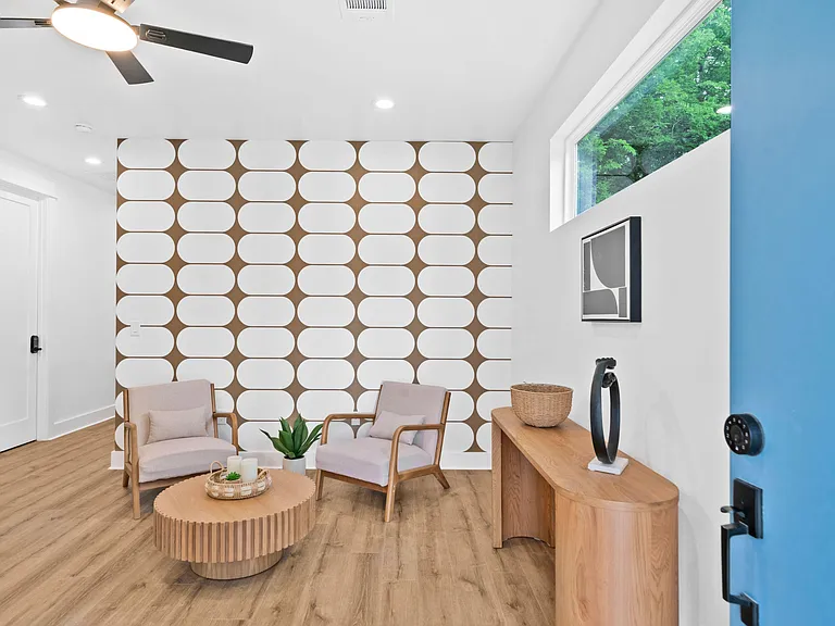 Stylish entry sitting area with two lounge chairs, accent wall, ceiling fan, and large window for natural light.