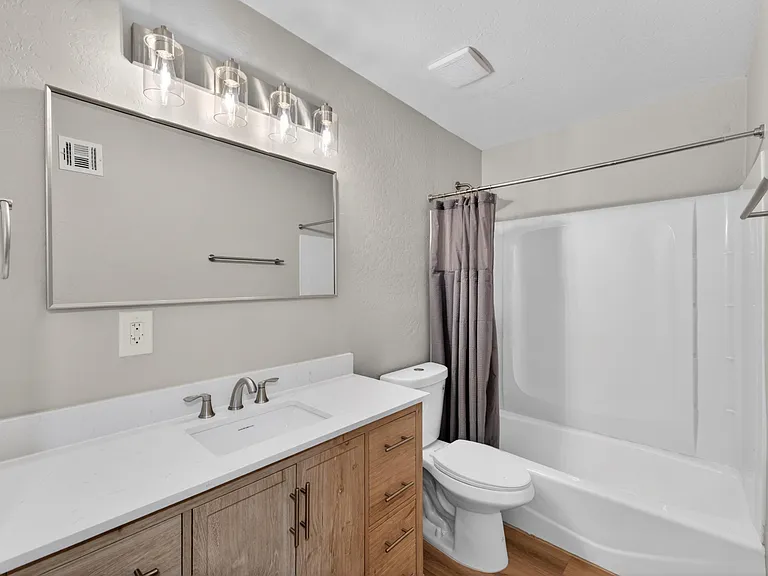 Full bathroom with wide vanity, large wall mirror, and a tub/shower combo with curtain rod for easy daily use.