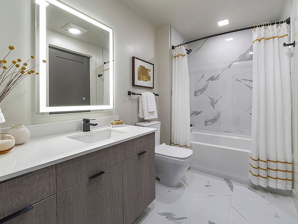 Apartment bathroom with large soaking tub, tile flooring, and LED vanity mirror.