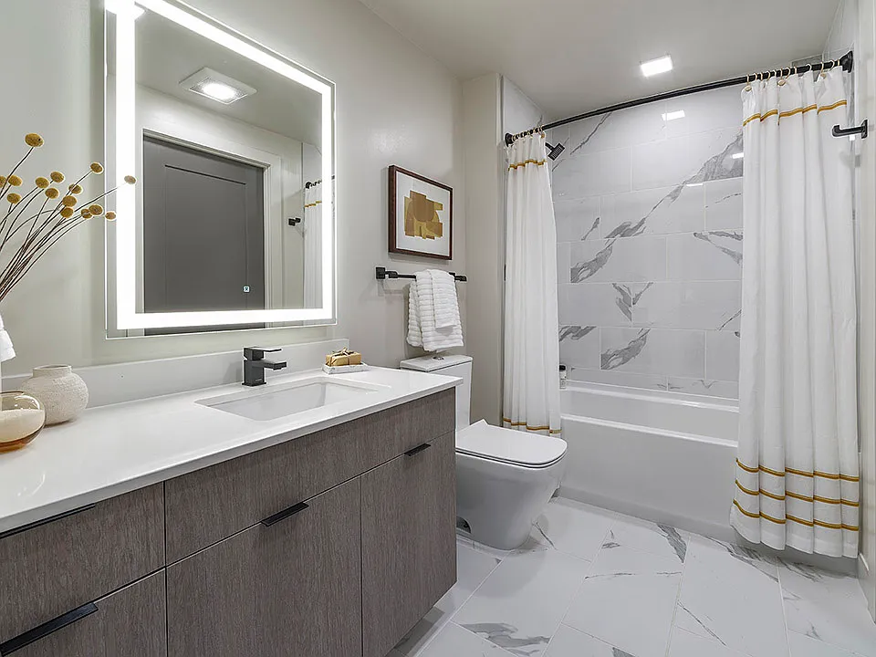Apartment bathroom with large soaking tub, tile flooring, and LED vanity mirror.