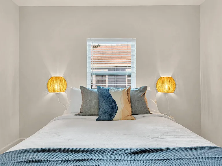 Bedroom with centered window, wall-mounted reading lights, and ample space for a full/queen bed and nightstands.