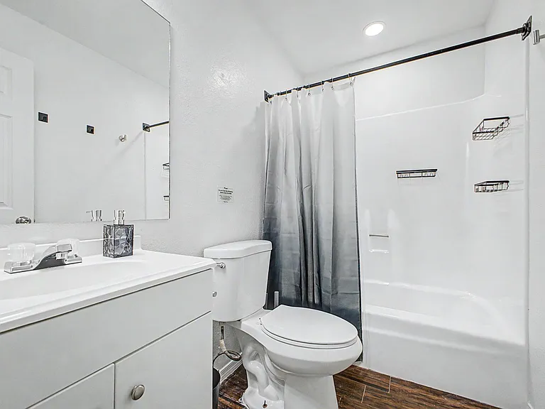 Clean full bathroom with a single-sink vanity, large mirror, and tub/shower combo with built-in shelving for toiletries.
