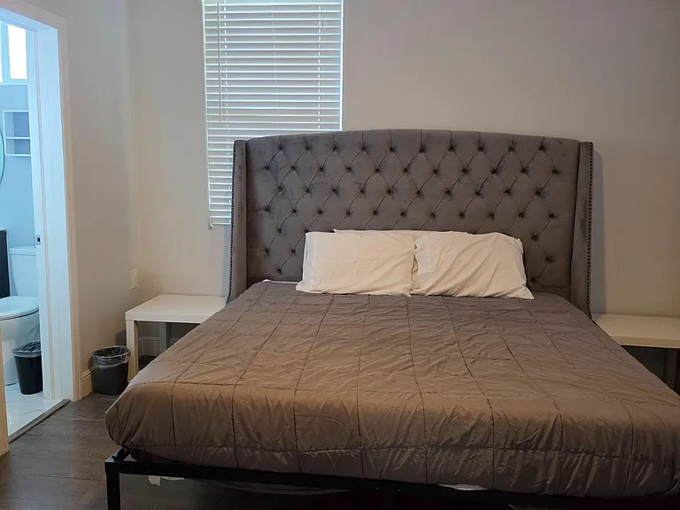 Private bedroom featuring a queen bed with tufted headboard, bedside tables, and a window with blinds for light control.