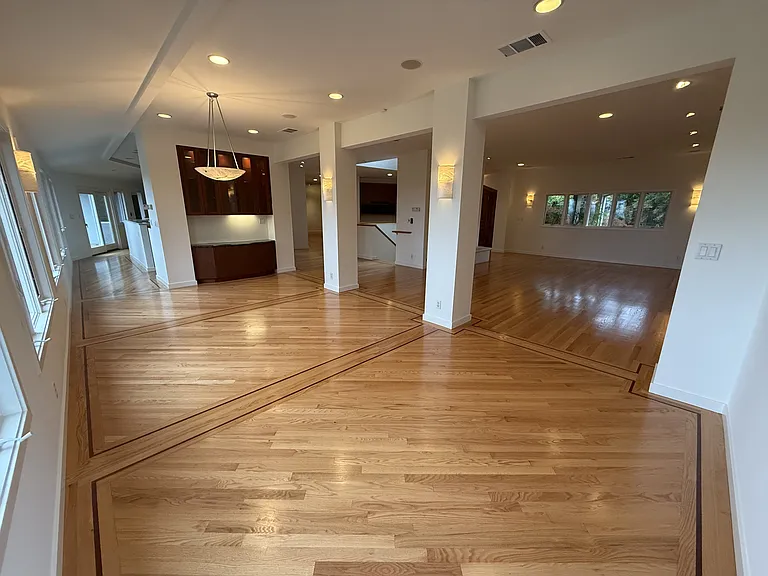 Grand living room and formal dining room featuring a fireplace, built-in buffet cabinetry, recessed lighting, rich wood flooring throughout and a wall of glass panels showcasing the bay view.