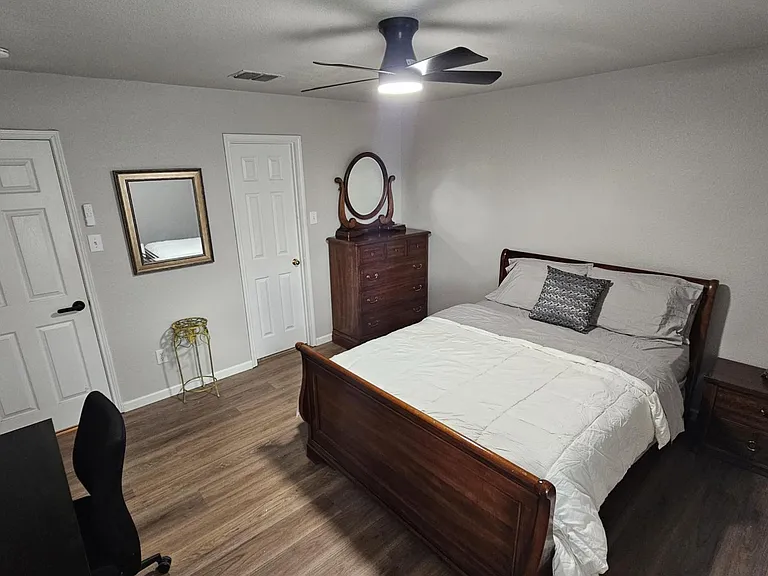 Furnished bedroom featuring a full bed, dresser and nightstand, plus a desk area and overhead ceiling fan light.