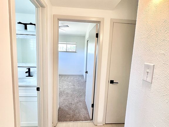 Bright hallway with modern light fixtures leading to carpeted bedroom and sleek bathroom, showcasing stylish finishes.