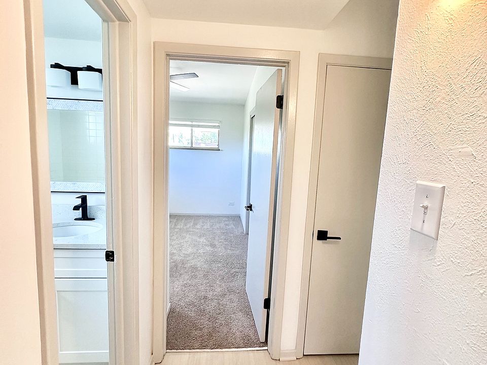 Bright hallway with modern light fixtures leading to carpeted bedroom and sleek bathroom, showcasing stylish finishes.
