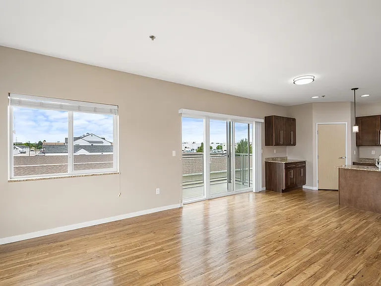 Bright open-concept kitchen and living area featuring modern appliances, hardwood floors, and large windows with balcony access. Bright open-concept kitchen and living area featuring modern appliances, hardwood floors, and large windows with balcony acces