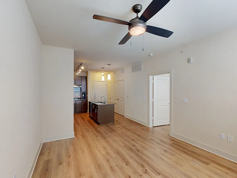 Apartment kitchen with stainless steel appliances, dining and living room with wood-style flooring.