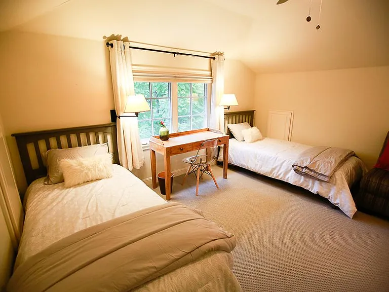 Upstairs bedroom #2 features two extra-long single beds with headboard frame that are long enough to accommodate adults. Each side has an adjustable wall-mounted lamp and plugs for charging. The desk area sits in front of a large double-window that overlo