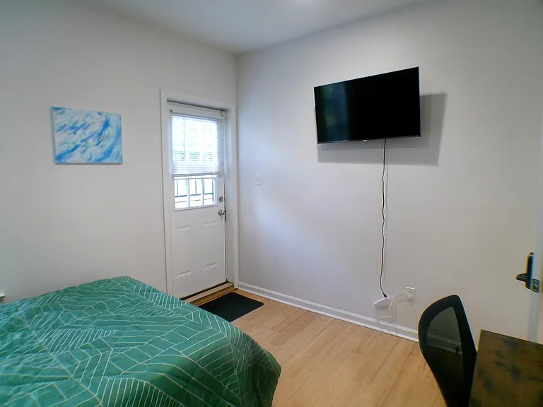 Private bedroom with wood-style flooring, a mounted TV, and a door with window blinds for convenient access and light.