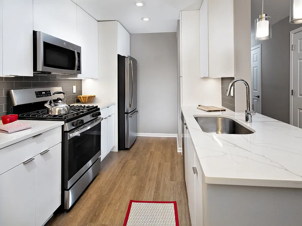 Premier Scheme kitchen with flat white cabinetry, white marbled quartz countertops, grey subway tile backsplash, stainless steel appliances, and hard surface flooring