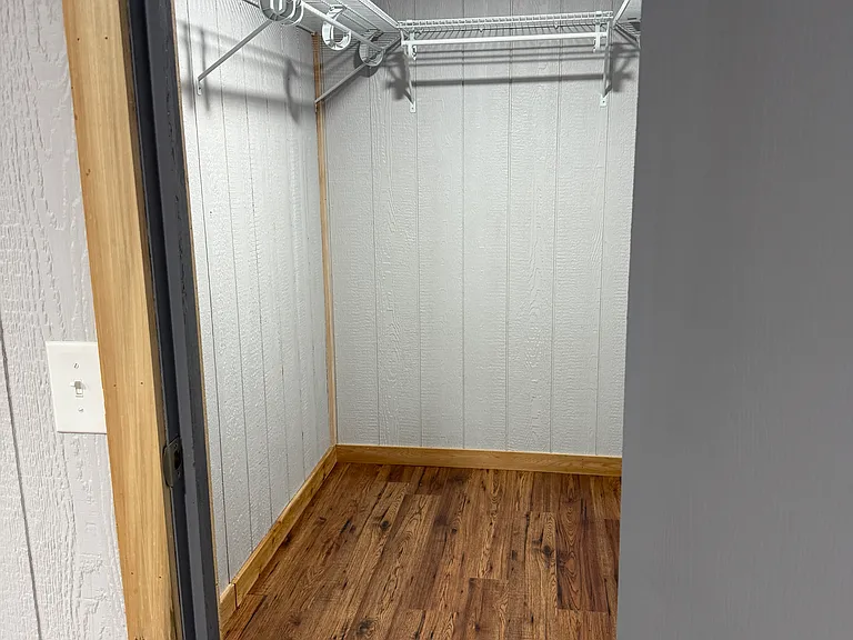 Master bedroom walk-in closet with U- shaped hanging shelves and shoe rack on the floor.