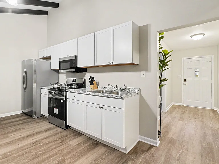 Galley-style kitchen with ample white cabinetry, granite-look counters, double-basin sink, and stainless appliances.