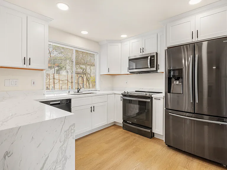 Stunning brand-new kitchen with sleek stainless steel appliances, a spacious island bar for seating, and a stylish waterfall stone countertop design that adds a luxurious touch.