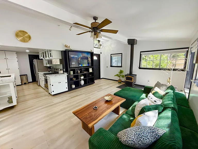 Open-concept living area with large windows, ceiling fan, and seating space flowing into a well-equipped kitchen.