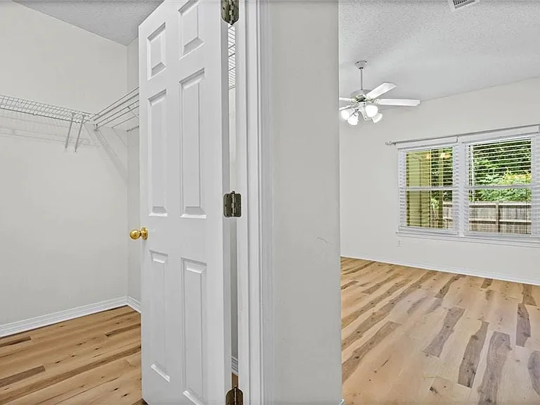 Bedroom with wood-finish flooring, a ceiling fan, and a large window with blinds