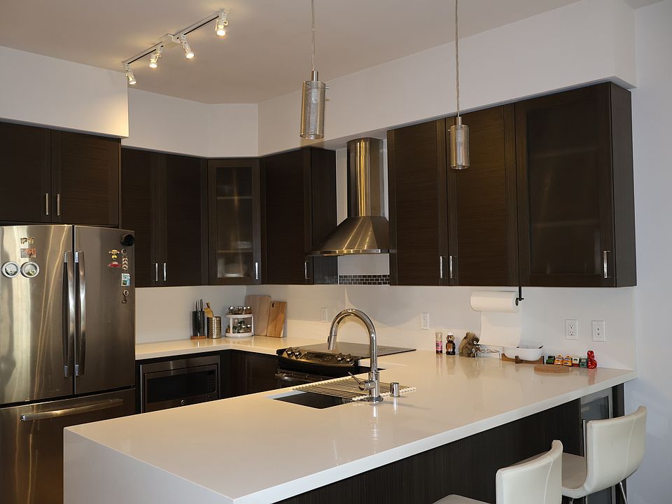 Kitchen, fully equipped with stainless steel appliances, including a French-door refrigerator, built-in microwave, electric cooktop, and a premium range hood, paired beautifully with clean white quartz countertops.