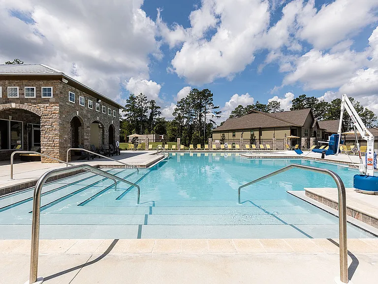 Inviting swimming pool with crystal-clear water, surrounded by stone buildings and lush greenery under a bright blue sky, perfect for relaxation and leisure.