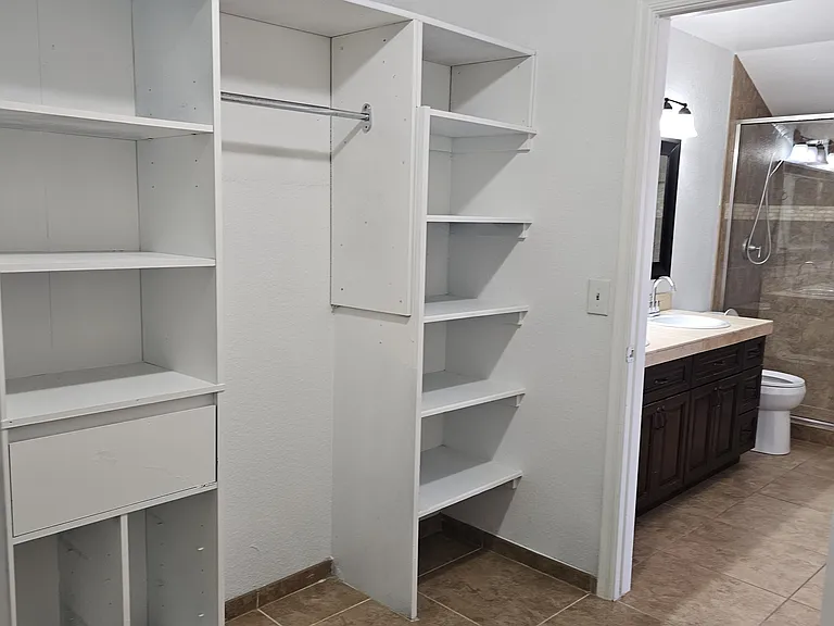 Spacious primary closet with built-in shelving and direct access to the en-suite bathroom, offering excellent storage and convenience.