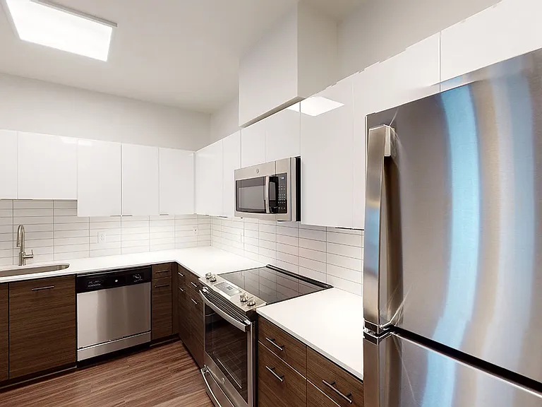 Apartment kitchen with stainless steel appliances, quartz countertops and wood-style flooring.