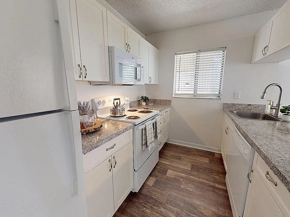Modern kitchen with sleek white cabinetry, granite countertops, and stainless steel appliances, offering a stylish and functional space.