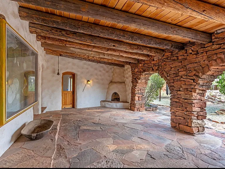 On the back side of property extra large covered portal with Kiva fireplace, random natural stone floor and arched mossrock stone Pilars