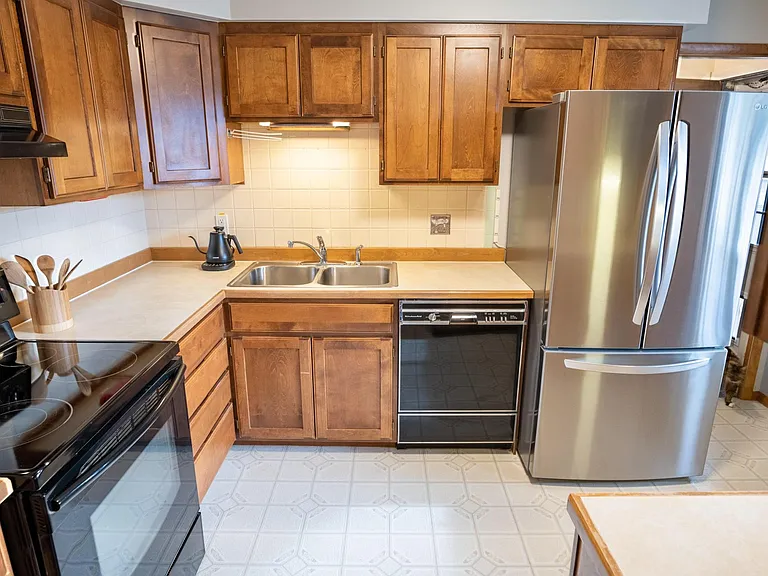 Kitchen with stove, cabinets, sink, dishwasher, and refrigerator. The passage on the right side of the refrigerator leads to the sun room, garage, and basement stairs.
the refrigerator is a modern refrigerator with French doors and bottom freezer drawer.
