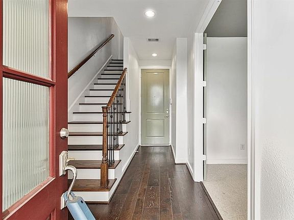 This is a welcoming entryway featuring a red door, surrounded by attractive exposed brickwork. The residence has well-maintained greenery by the door, adding to the home's curb appeal.