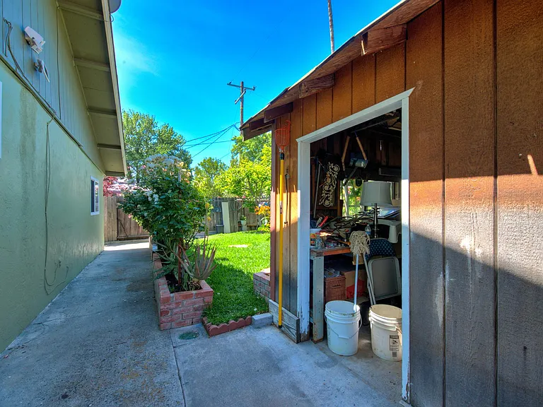 Walkway between west side of the house and shed. Back yard and lawn in the distance.