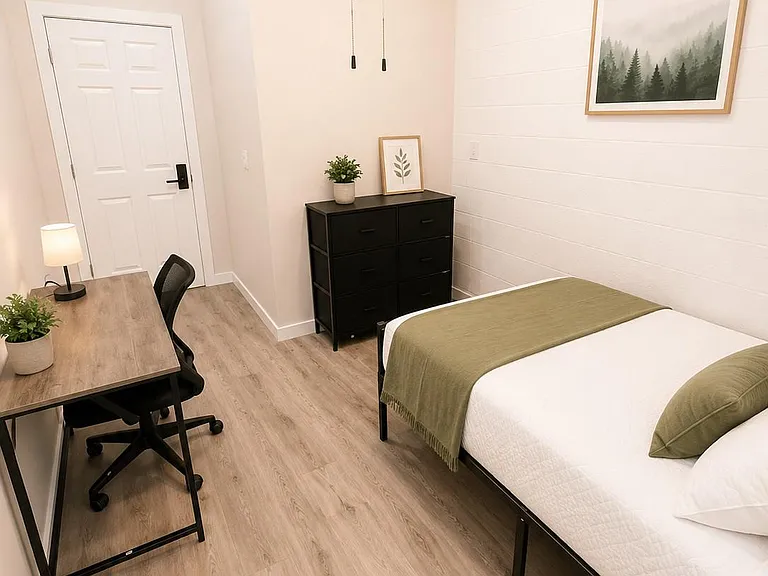 Private bedroom with wood-look flooring, a full bed, dresser storage, and a dedicated desk area for studying or work.