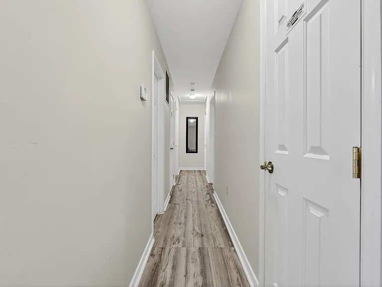 Long interior hallway with durable wood-look flooring, multiple room access doors, and overhead lighting for easy navigation.