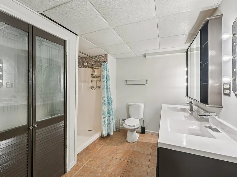 A spacious lower level bathroom with double vanity sinks, warm tile flooring, and a walk in shower, creating a practical retreat with a touch of hidden charm.