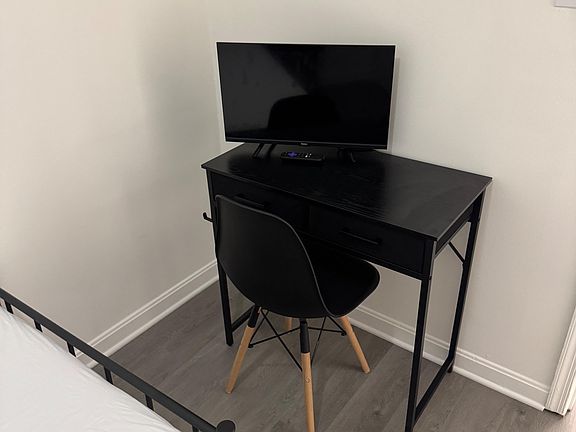 Bedroom work nook featuring a dedicated desk with chair and a TV setup, plus durable flooring and clean wall space.