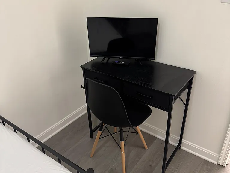 Bedroom work nook featuring a dedicated desk with chair and a TV setup, plus durable flooring and clean wall space.