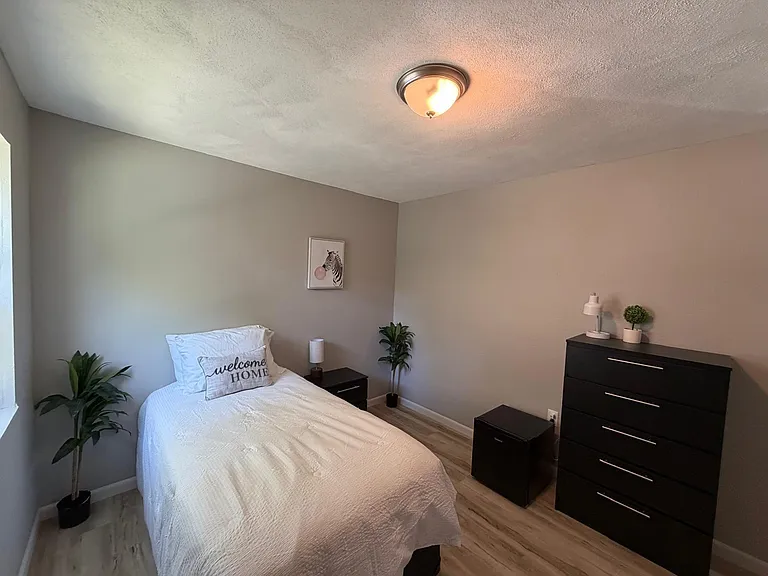 Well-appointed bedroom featuring a comfortable bed, nightstand, dresser storage, and wood-look flooring with neutral tones.