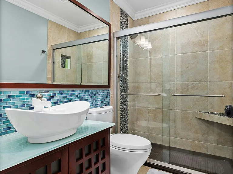 Modern and refreshing this full bathroom features a sleek vessel sink, mosaic tile detail, and a glass-enclosed shower with built-in seating for a spa-like touch.