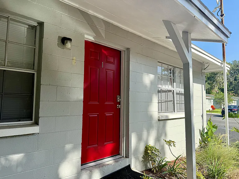 Inviting apartment entrance with a bold red door, surrounded by lush greenery and ample natural light.