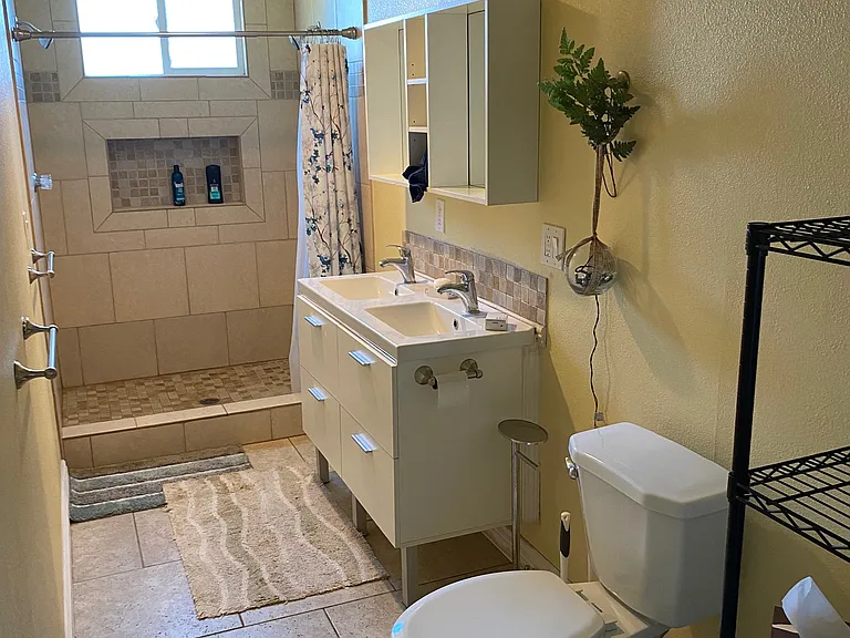 Bathroom with double vanity, double shower heads. Storage shelving.