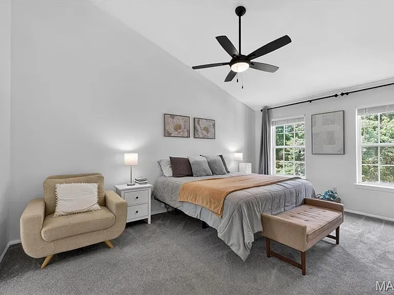 Spacious room featuring vaulted ceilings, a ceiling fan with integrated lighting, two large windows, and neutral carpeting