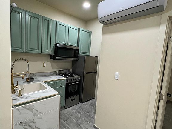 Compact, fully equipped kitchen with a gas stove and oven, overhead microwave, and apartment-sized refrigerator_all kept comfortable by a wall-mounted mini-split (AC/Heating all in one) system.