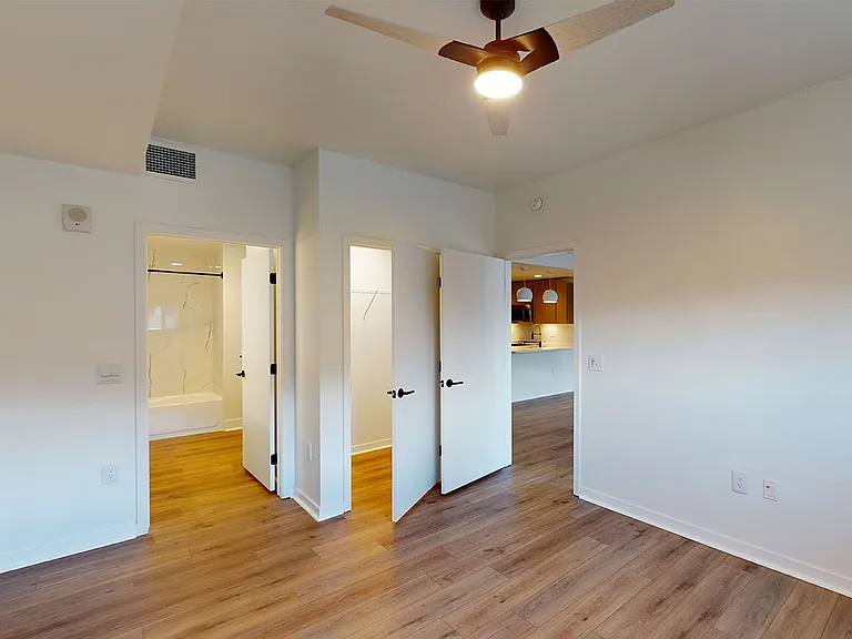 Spacious apartment bedroom with large closet, attached bathroom and wood-style flooring.