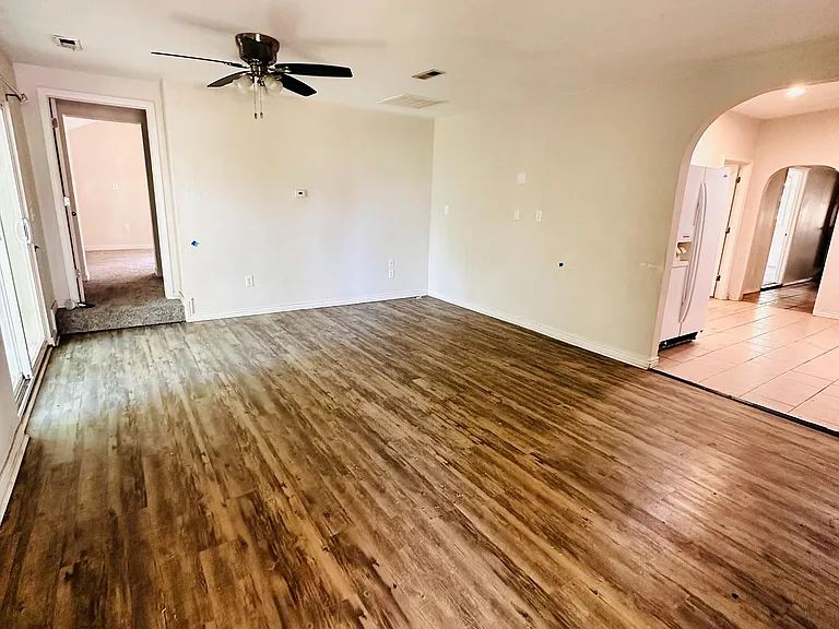 Inviting living area with elegant wooden flooring, ceiling fan, and archway leading to a bright kitchen.
