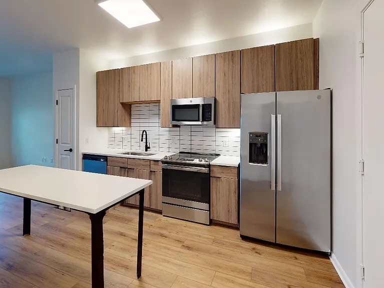 Apartment kitchen with stainless steel appliances, quartz countertops and wood-style flooring.