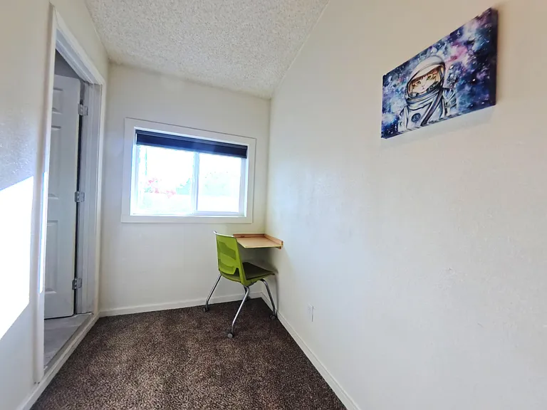 Compact room with carpet flooring, a window for daylight, and a wall-mounted desk nook for working or studying.