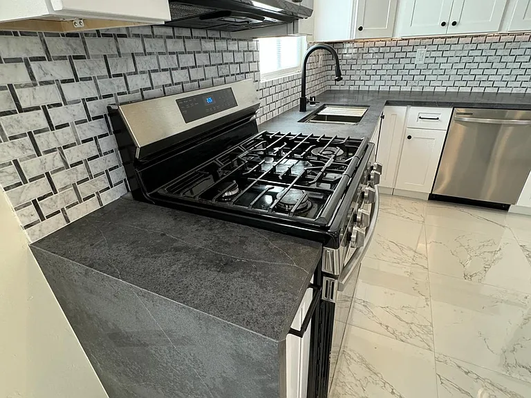 Kitchen with new SS appliances, quartz countertops, white shaker cabinets, workstation sink, island and under cabinet lighting. Gas stove.