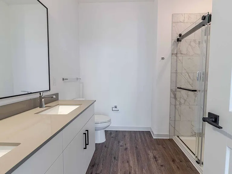 Primary bathroom featuring a dual-sink quartz vanity and a glass-enclosed walk-in shower with marble-style tile. Primary bathroom featuring a dual-sink quartz vanity and a glass-enclosed walk-in shower with marble-style tile.