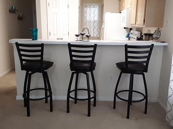 View of the Kitchen breakfast bar with 3 swivel stools and the hall leading to the front door on the left.