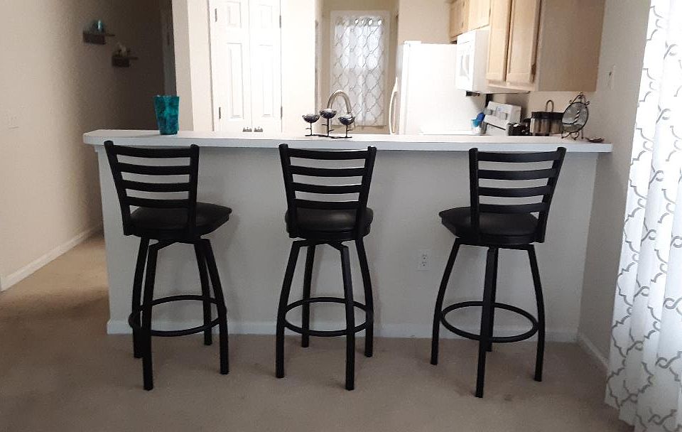 View of the Kitchen breakfast bar with 3 swivel stools and the hall leading to the front door on the left.